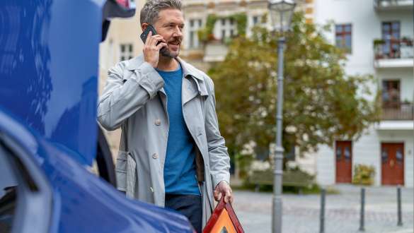 Un homme se tient devant le coffre de la BMW Série 5 Berline G30 Homme se tient devant le coffre de la BMW avec un téléphone portable et un triangle de signalisation dans les mains, BMW Série 5 Berline G30