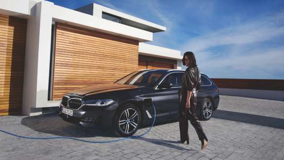 BMW Série 5 Touring 2021 G31 hybride rechargeable, vue de trois quart de profil, branchée à une borne de recharge BMW Série 5 Touring 2021 G31 hybride rechargeable, vue de trois quart de profil, branchée à une borne de recharge avec modèle