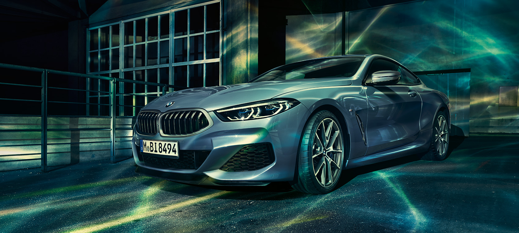 BMW Série 8, vue de trois quarts face La BMW Série 8 Coupé (F92) couleur Barcelona Blau Métallisé, de trois quarts face, à l'arrêt dans un décor urbain.