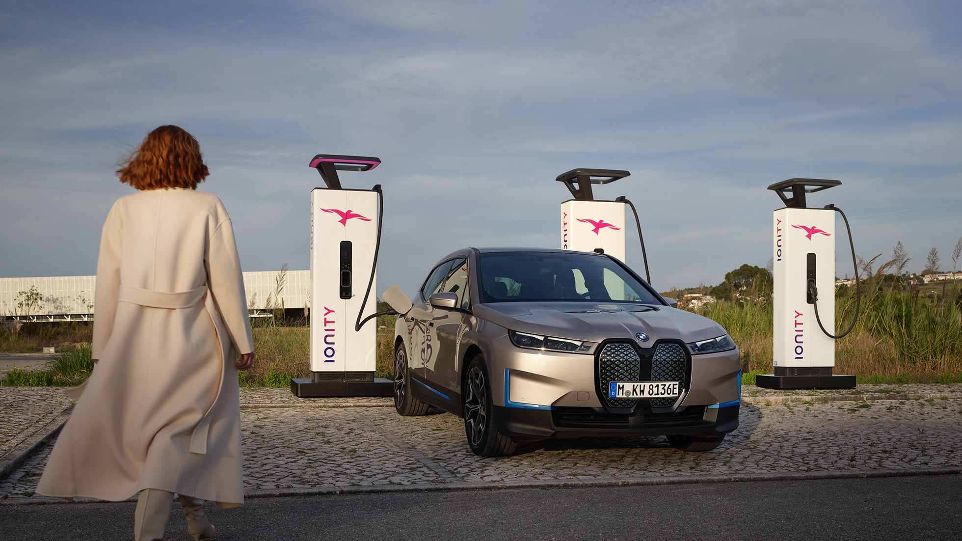 BMW iX vue de trois quarts avant sur une borne de recharge BMW iX Kaschmirsilber i20, vue de trois quarts avant sur une borne de recharge
