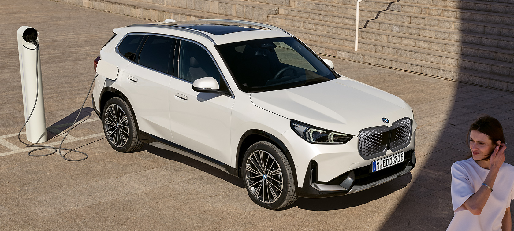 SUV compact électrique BMW iX1 U11 BEV vue de profil en charge SUV compact électrique BMW iX1 U11 BEV 2022 Mineralweiss metallisé vue de profil en charge près des escaliers