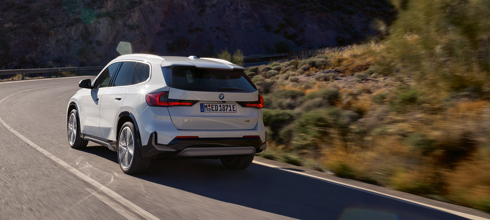 SUV compact électrique BMW iX1 U11 BEV dynamique de conduite aperçu vidéo SUV compact électrique BMW iX1 BEV 2022 Mineralweiss metallisé 2/3 vue arrière en mouvement sur route de montagne dynamique de conduite aperçu vidéo