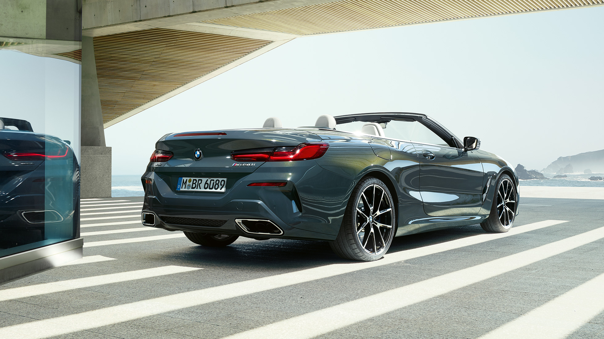 BMW M850i xDrive Cabriolet, vue de trois quarts arrière G14. BMW M850i xDrive Cabriolet en Dravitgrau metallic avec capote ouverte, vue de trois quarts arrière, en stationnement avec vue sur l’océan G14.