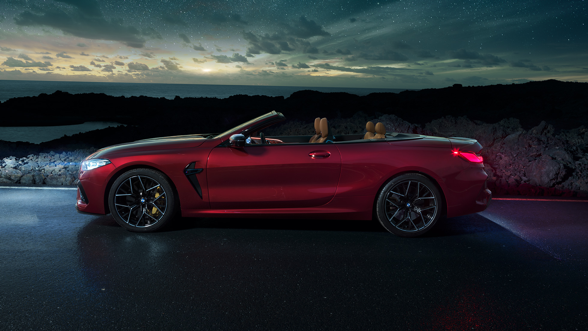 BMW M8 Competition Cabriolet, vue de profil F91. BMW M8 Competition Cabriolet en Motegi Rot metallic avec capote ouverte, vue de profil nocturne sous un ciel étoilé F91.