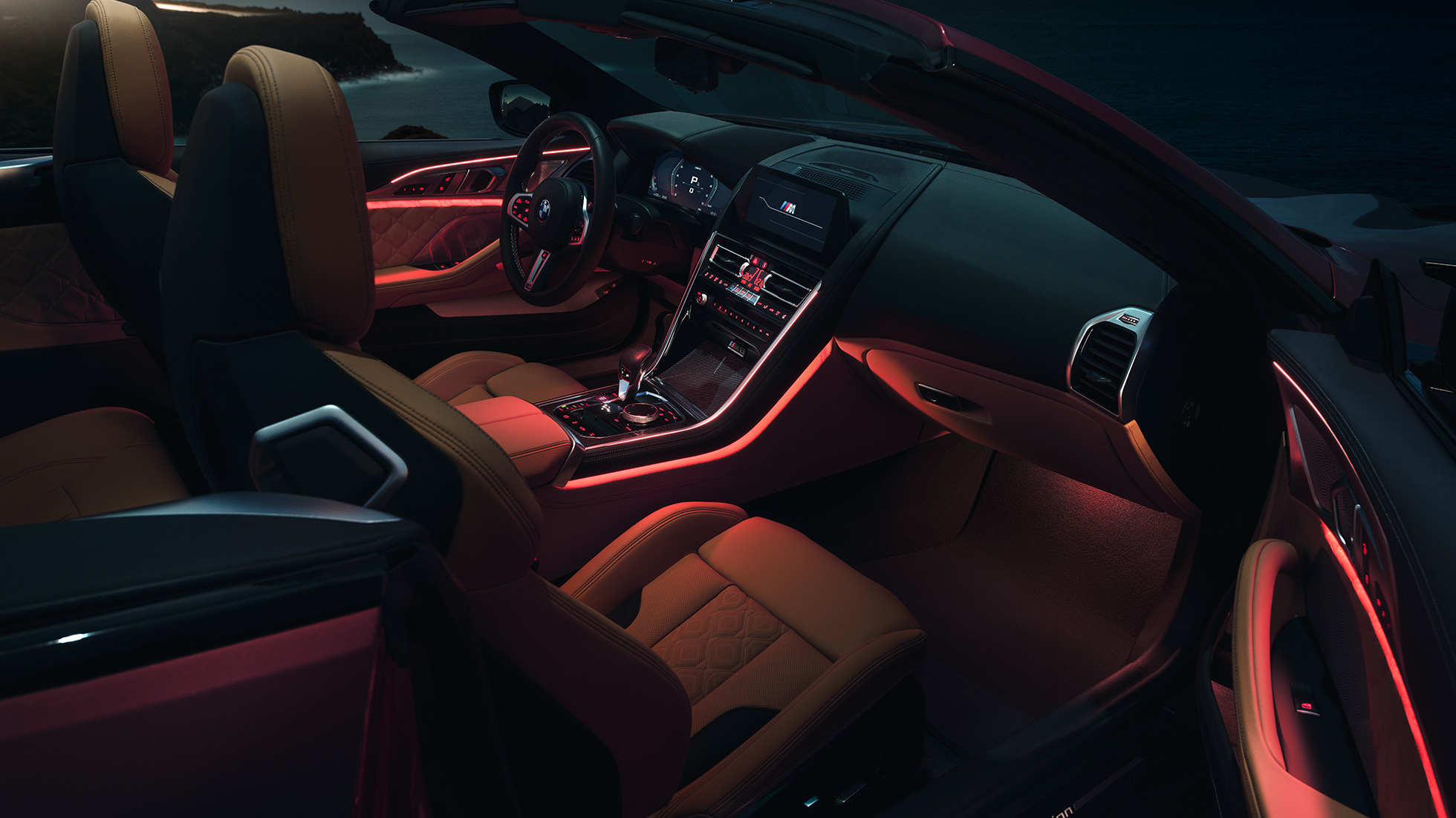 BMW M8 Competition Cabriolet, habitacle F91. BMW M8 Competition Cabriolet avec capote ouverte, prise de vue nocturne de l’habitacle avec éclairage d’ambiance rouge F91.