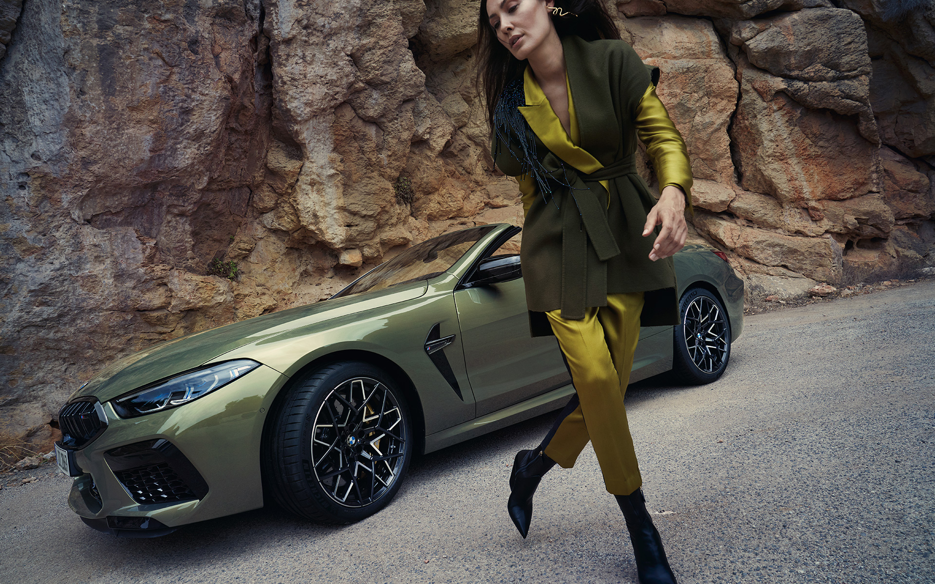 La nouvelle BMW M8 Competition Cabriolet F91 LCI restylage 2022 BMW Individual Brass metallic vue de trois quarts avant sur un terrain rocailleux avec mannequin féminin
