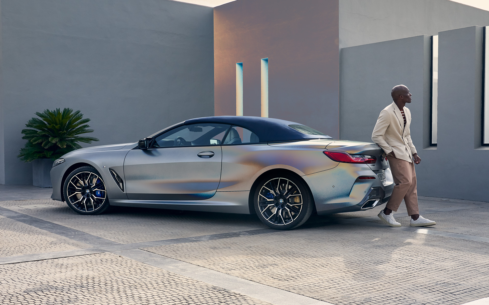 La nouvelle BMW M850i xDrive Cabriolet G14 LCI restylage 2022 BMW Individual Frozen Pure Grey metallic, vue de trois quarts arrière adossée au véhicule avec un modèle homme