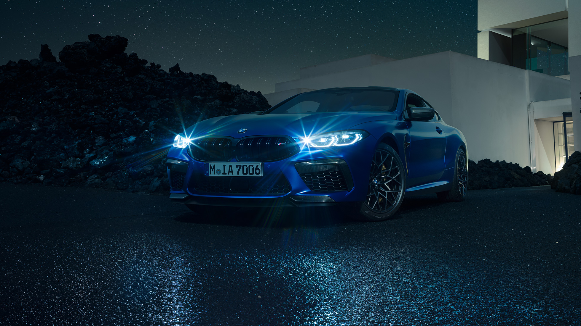 BMW M8 Competition Coupé, vue de trois quarts avant F92. BMW M8 Competition Coupé en Marina Bay Blau metallic avec phares LED allumés, vue de trois quarts avant à l’arrêt devant une villa, la nuit F92.