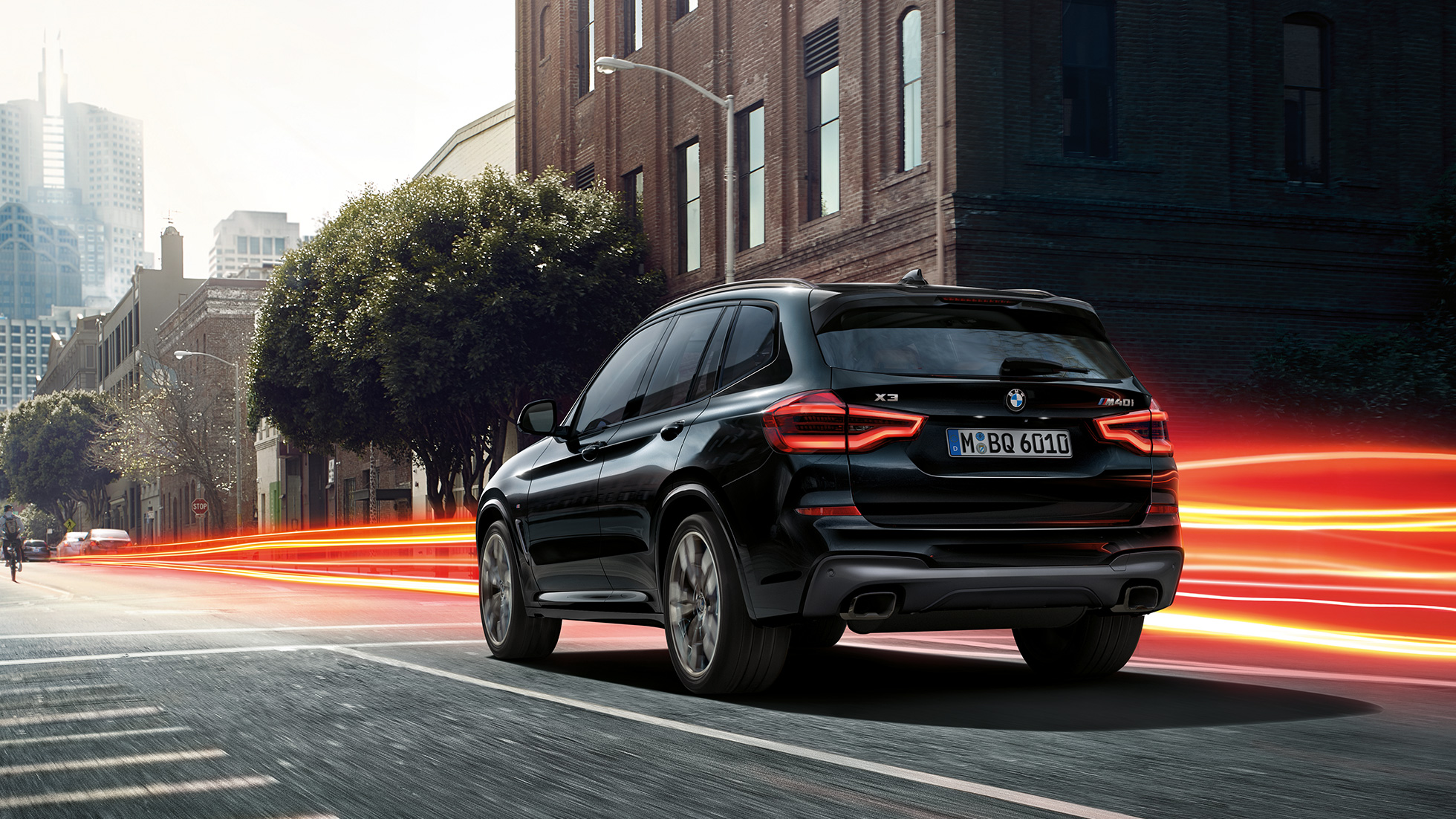 BMW X3 M40i, vue de trois quarts arrière Extérieur de la BMW X3 M40i en Saphierschwarz metallic, en mouvement, vue de trois quarts arrière devant un paysage urbain avec bandes lumineuses