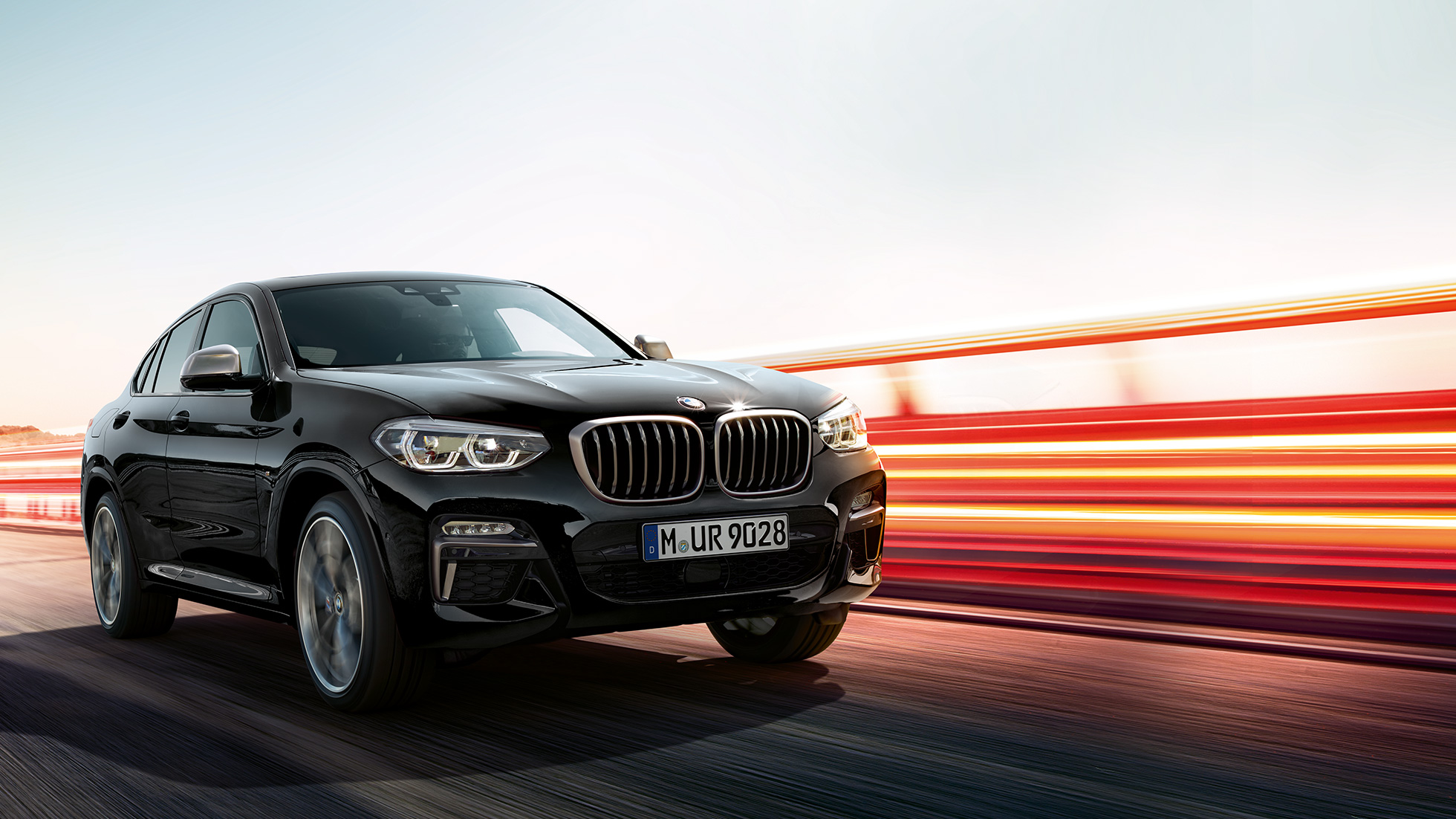 BMW X4 M40i, vue de trois quarts arrière G02. Extérieur de la BMW X4 M40i en Saphierschwarz metallic, en mouvement, vue de trois quarts arrière avec bandes lumineuses G02.
