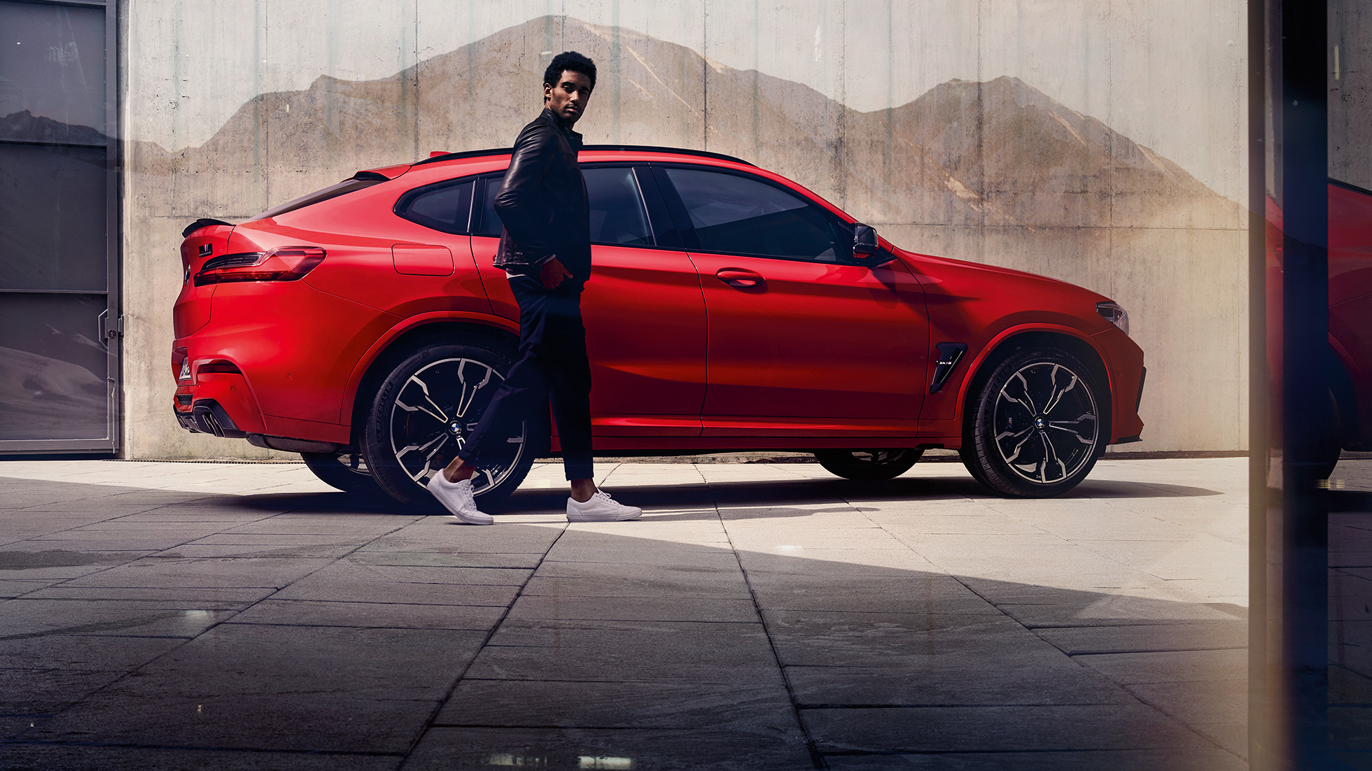 BMW X4 M Competition, vue de profil avec jeune homme F98. Extérieur de la BMW X4 M Competition en Toronto Rot metallic, vue de profil avec jeune homme F98.