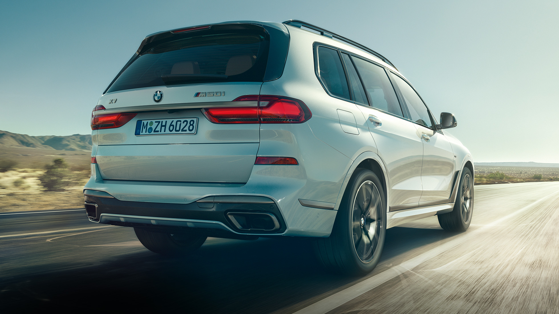 BMW X7 M50i blanc vue trois quart arrière BMW X7 M50i vue de trois quart arrière en dynamiqe sur la route
