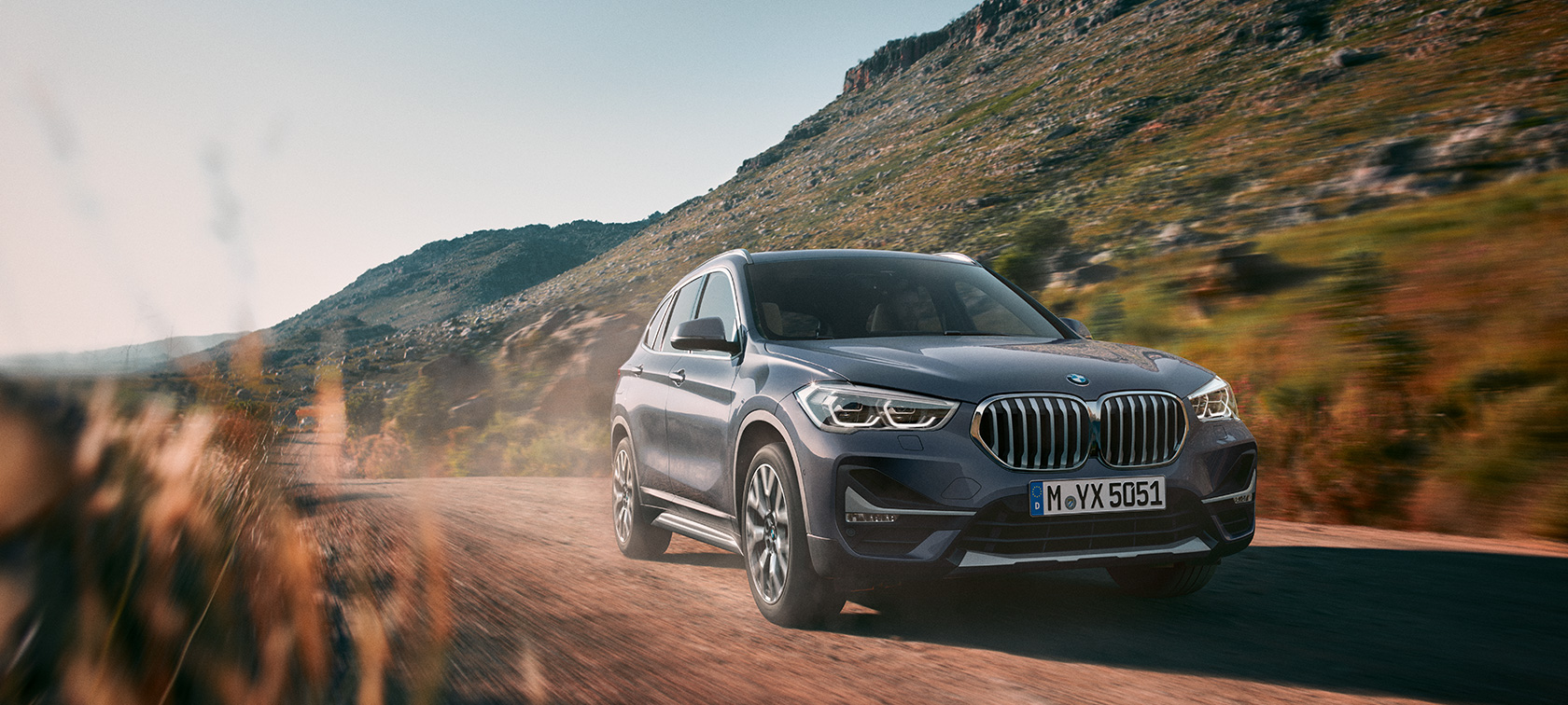 BMW X1 (F48) Storm Bay metallisé, vue trois quart avant, conduite en montagne. BMW X1 (F48) Storm Bay metallisé, vue trois quart avant, conduite en montagne.