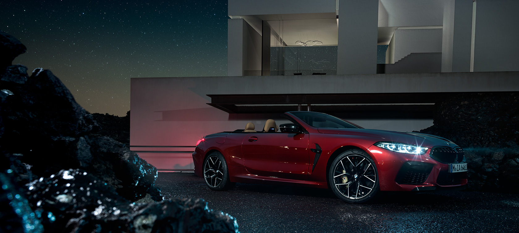 BMW M8 Competition Cabrio en Motegi Rot metallic, vue de trois quarts de profil, à l’arrêt devant une villa, de nuit. BMW M8 Competition Cabrio en Motegi Rot metallic, vue de trois quarts de profil, à l’arrêt devant une villa, de nuit.