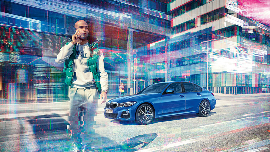 BMW bleue avec homme au téléphone Homme téléphonant avec son GSM, avec en arrière-plan une BMW bleue devant un décor urbain.