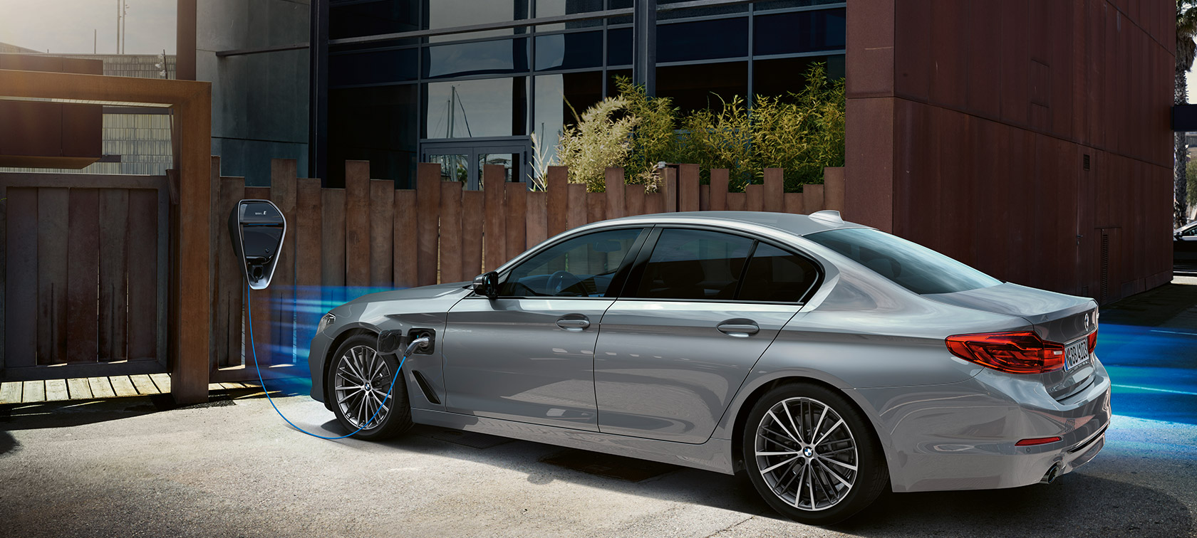 BMW 530e devant borne de recharge. BMW 530e vue de trois quarts arrière, près de la borne de recharge.