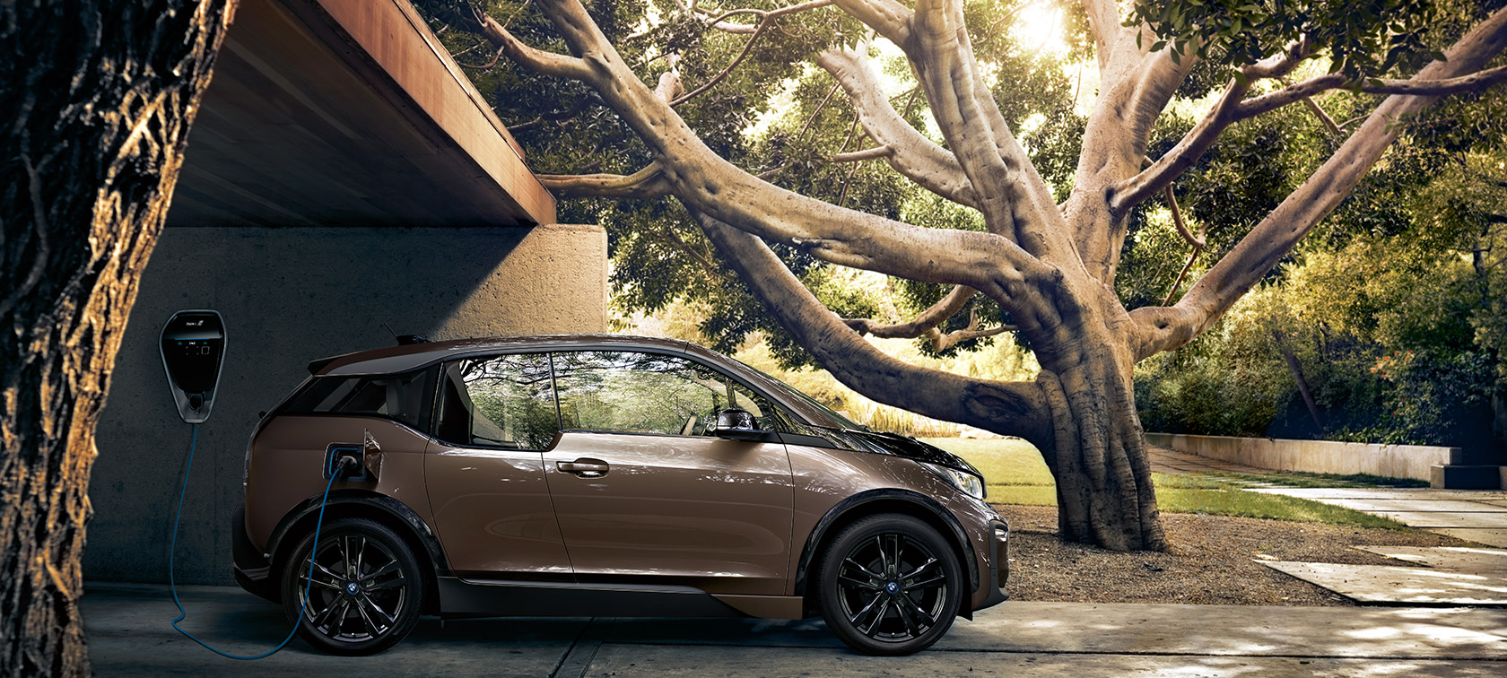BMW i3s branchée à la BMW i Wallbox. BMW i3s vue de profil et branchée à la BMW i Wallbox dans un décor naturel.
