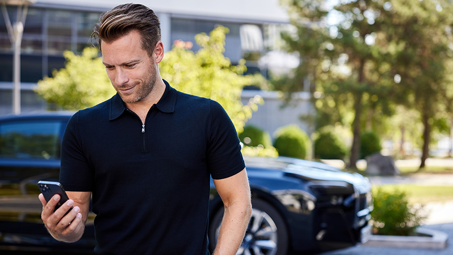 BMW Online Genius Homme équipé d’un smartphone devant une BMW