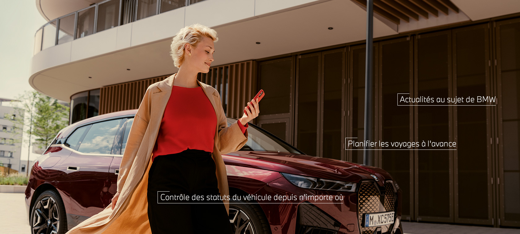 Femme devant la BWW iX qui utilise l'App My BMW sur smartphone. Femme devant la BWW iX qui utilise l'App My BMW sur Smartphone