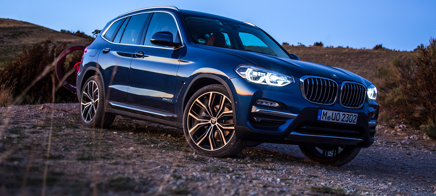 BMW X3 bleu foncé dans la nature BMW X3 bleu foncé à l'arrêt avec porte-vélos et VTT dans la nature.