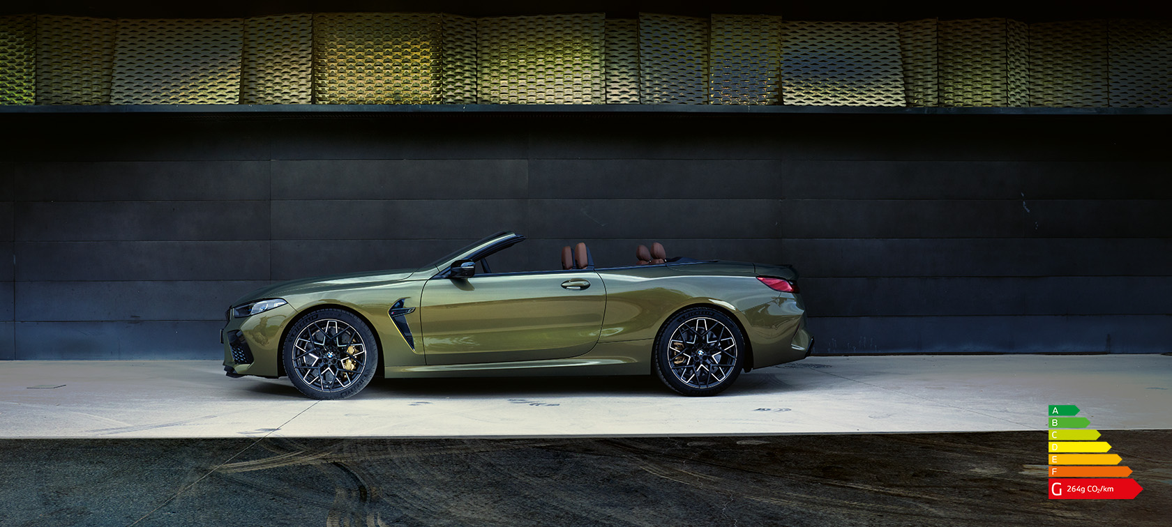 La BMW M8 M Competition Cabrio F91 LCI restylage 2022 BMW Individual Brass metallic Vue de profil en stationnement avec portière ouverte et mannequin femme