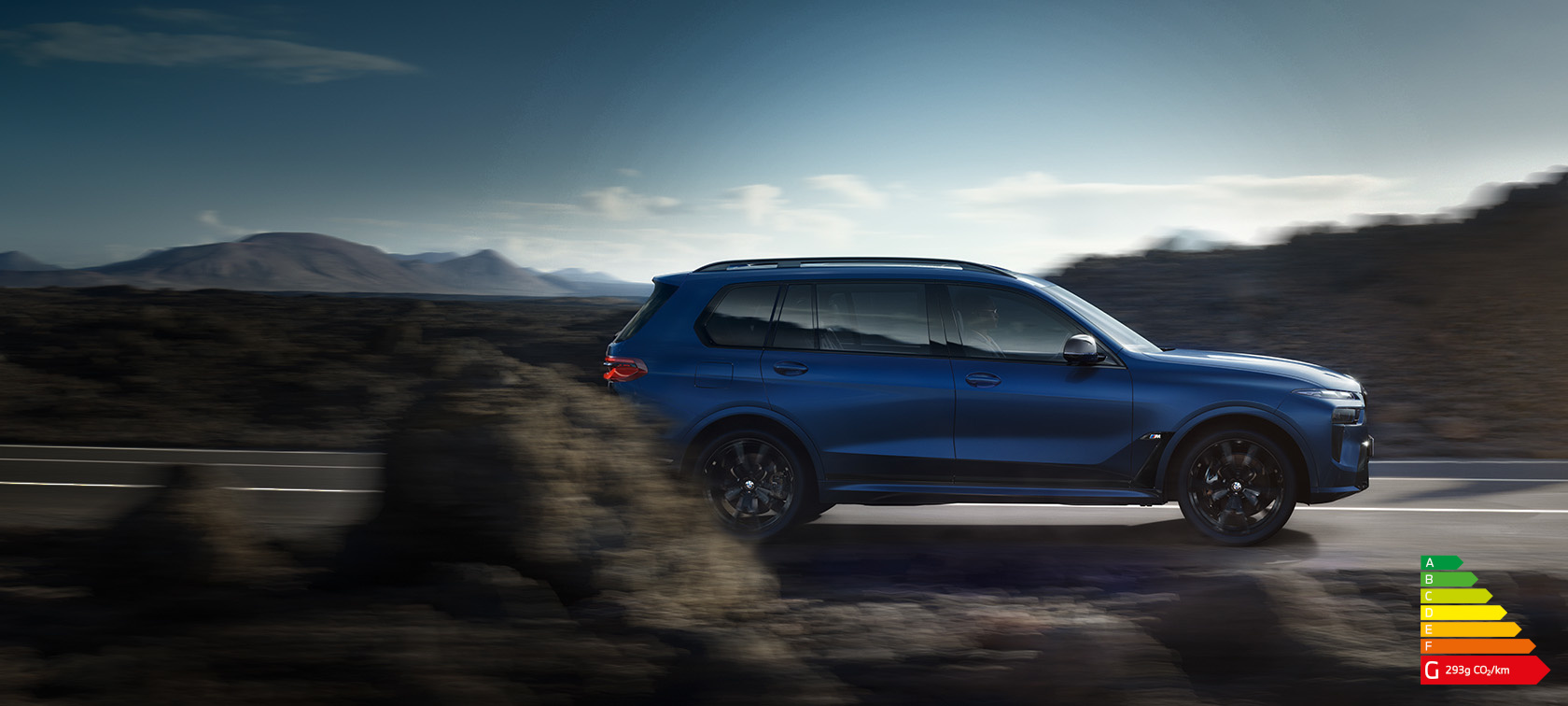 BMW X7 M60i xDrive G07 LCI Frozen Marina Bay Blue vue de profil roulant sur la route devant un paysage de montagnes