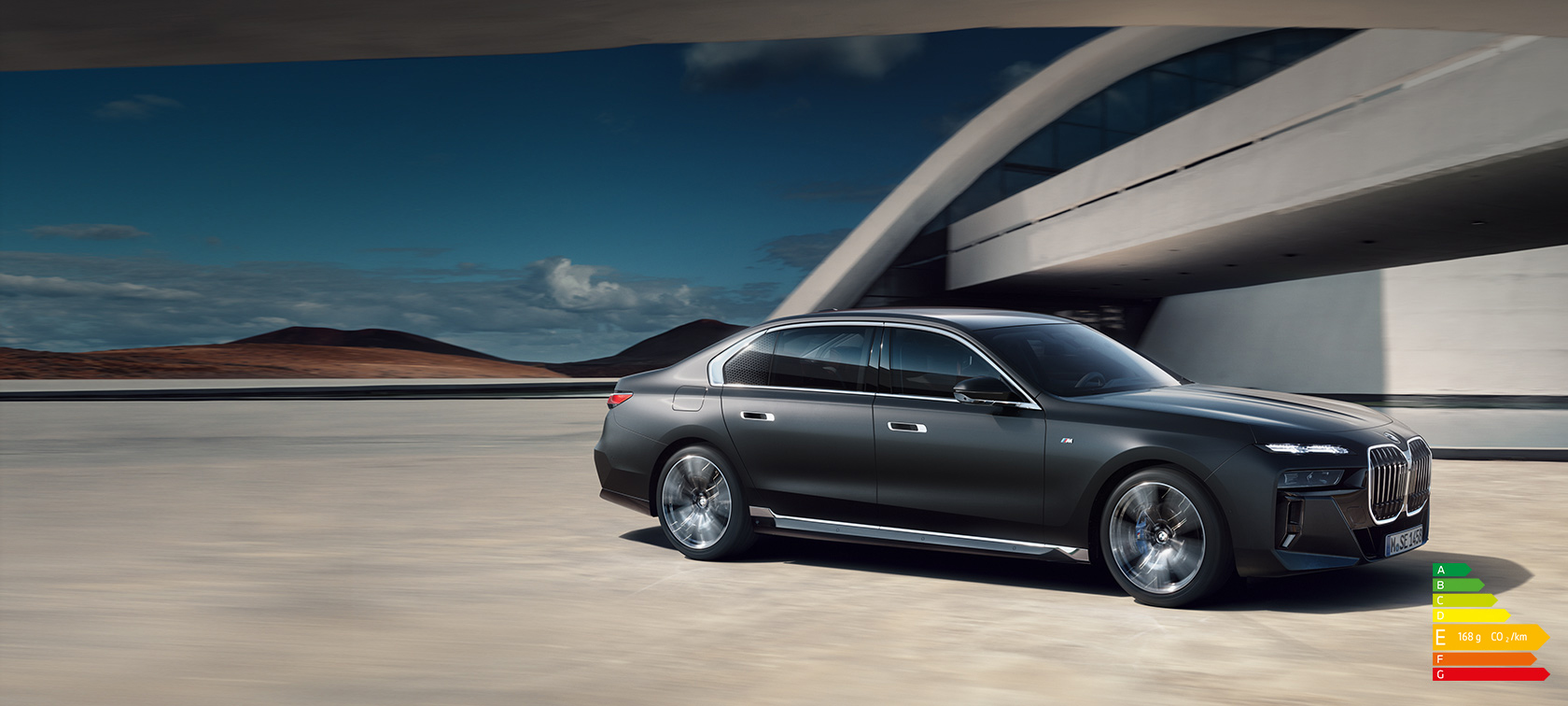 BMW Série 7 Berline G70 ICE kit M Sport Frozen Deep grey metallic vue ¾ face à l’arrêt devant un bâtiment