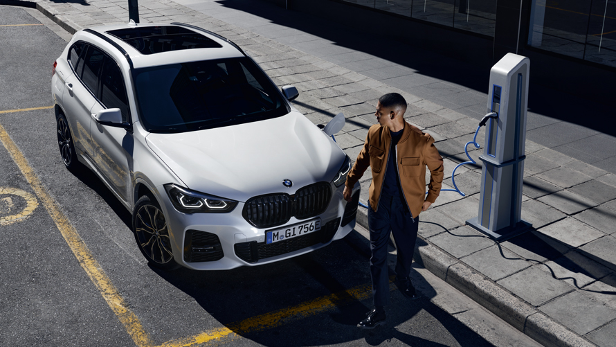 BMW X1 Hybride Rechargeable blanc garé en ville avec une figurante BMW X1 Hybride Rechargeable blanc garé en ville avec une figurante