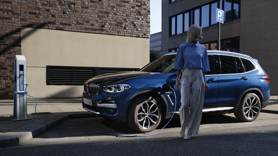 BMW X3 Hybride Rechargeable blanc garé dans la rue avec un figurant BMW X3 Hybride Rechargeable blanc garé dans la rue avec un figurant