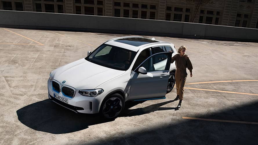 BMW iX3 blanche avec sa conductrice portière ouverte BMW iX3 blanche avec sa conductrice portière ouverte