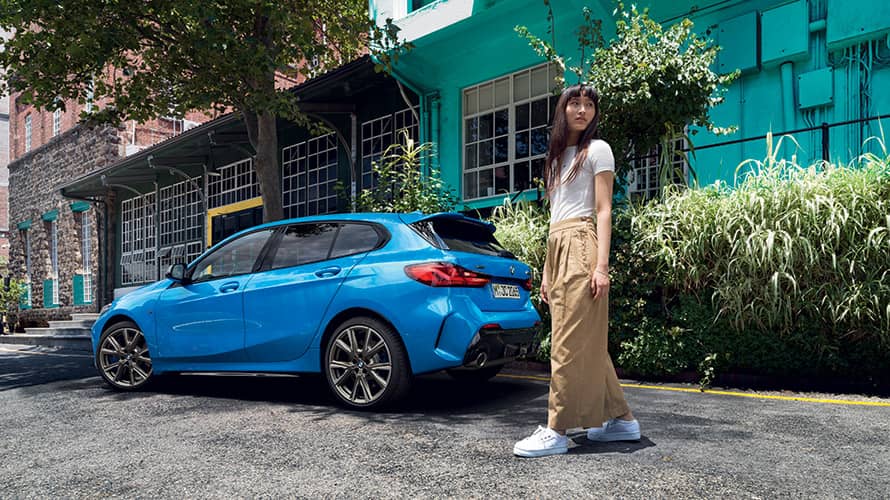 BMW Série 1 bleue de trois quart arrière avec une femme BMW Série 1 bleue de trois quart arrière avec une femme