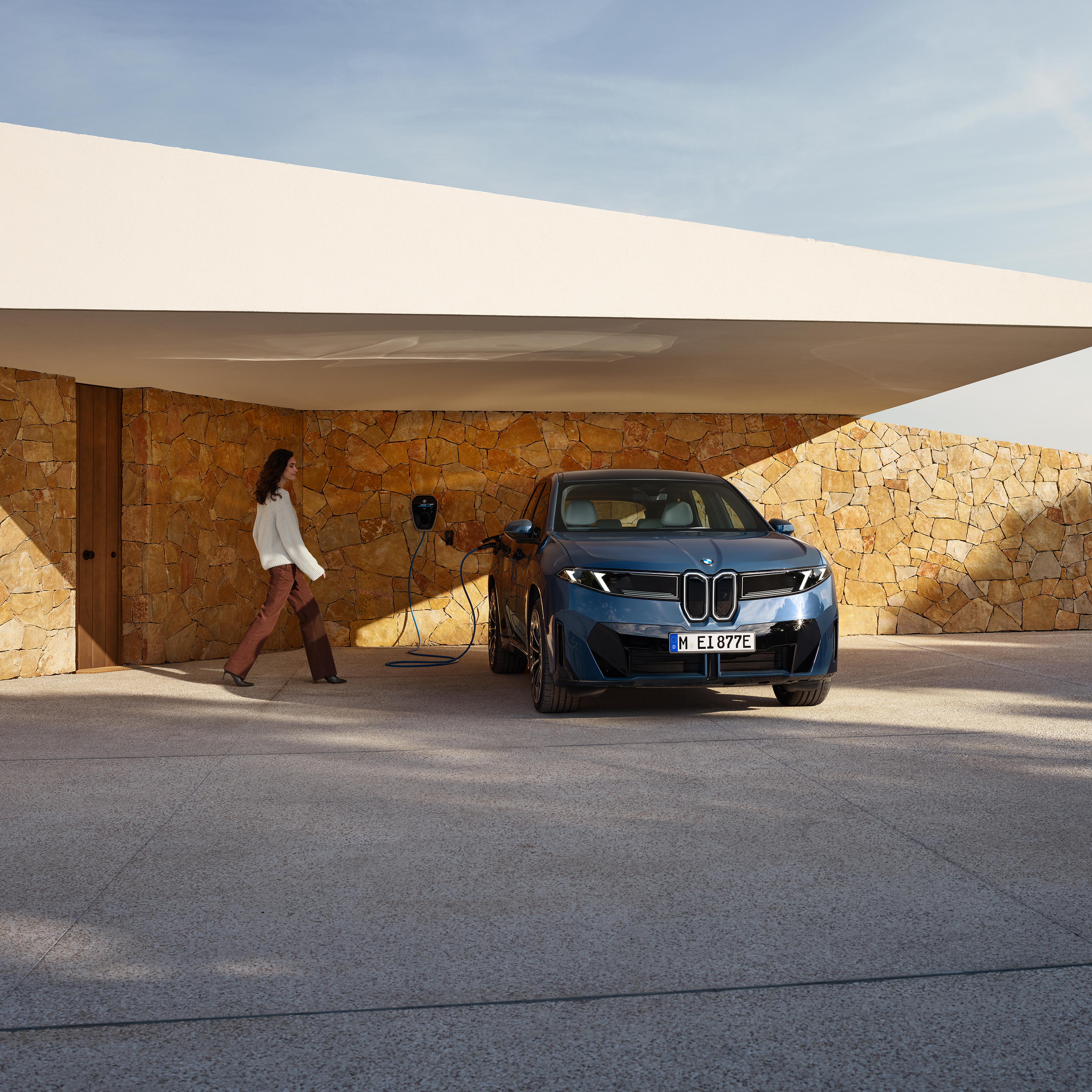 Une femme s'approche d'une BMW iX3 connectée à une wallbox