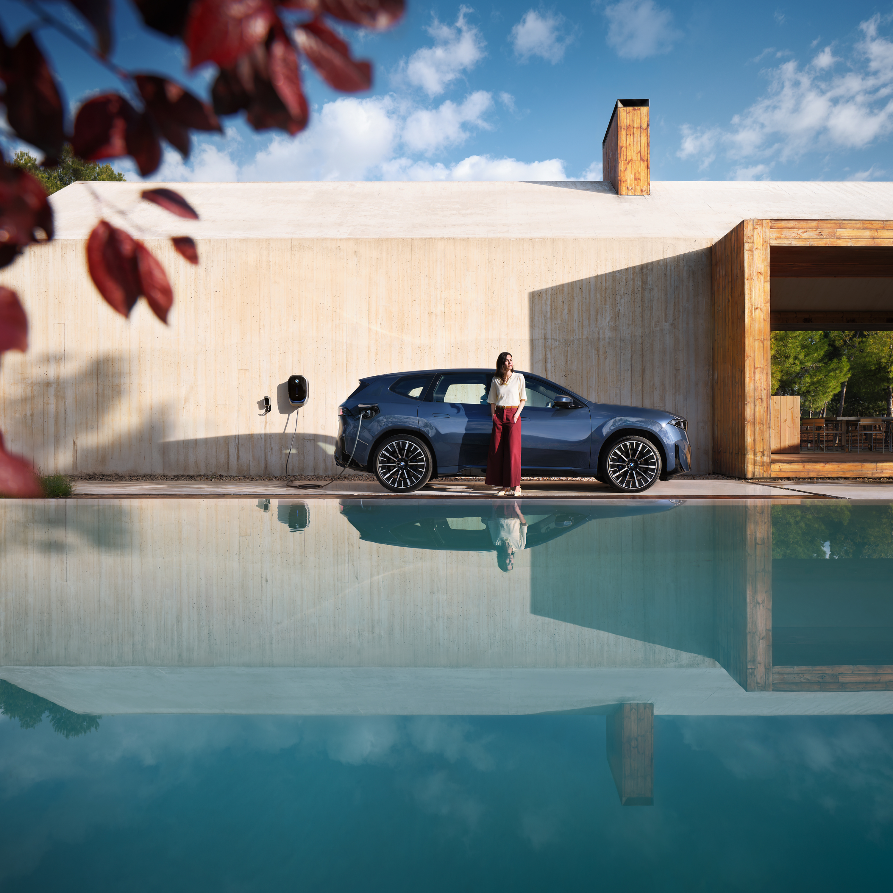 Une femme se tient devant une BMW iX3 connectée à une wallbox