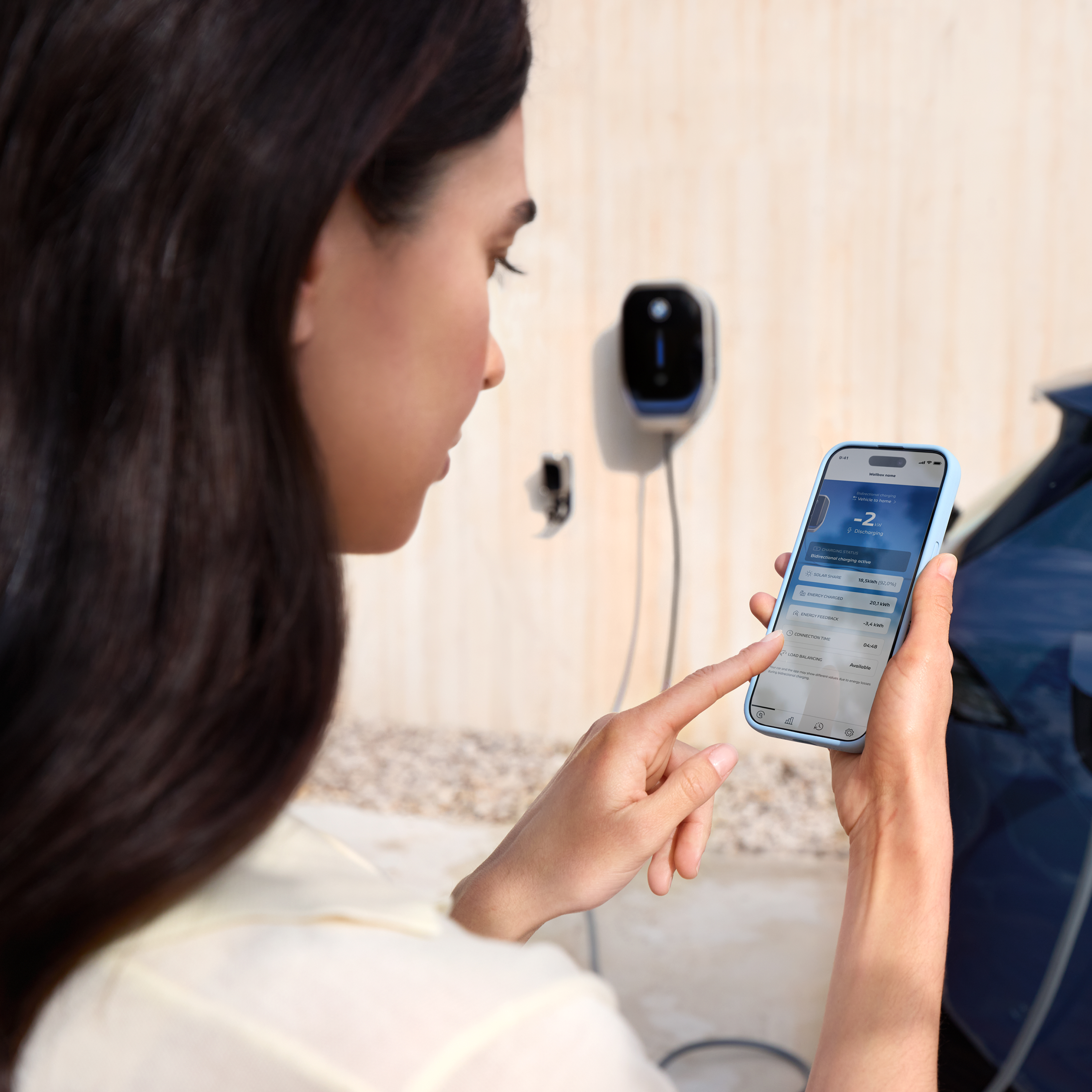 Une femme regarde son smartphone avec une wallbox BMW en arrière-plan
