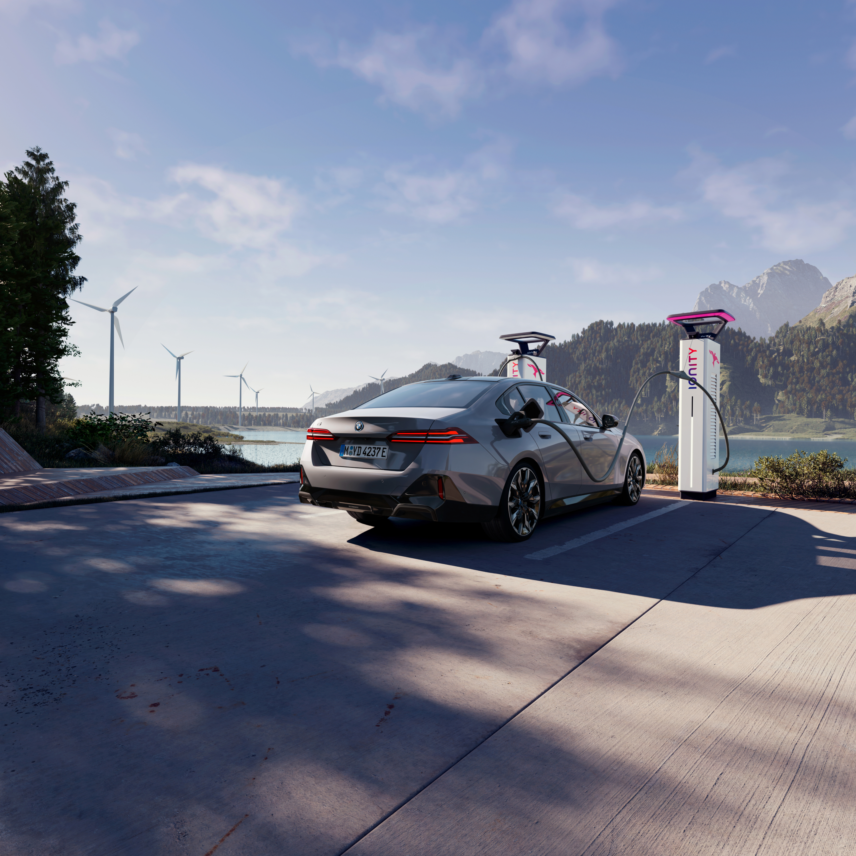 Une BMW se recharge à une borne avec vue sur l’eau, les montagnes et des éoliennes